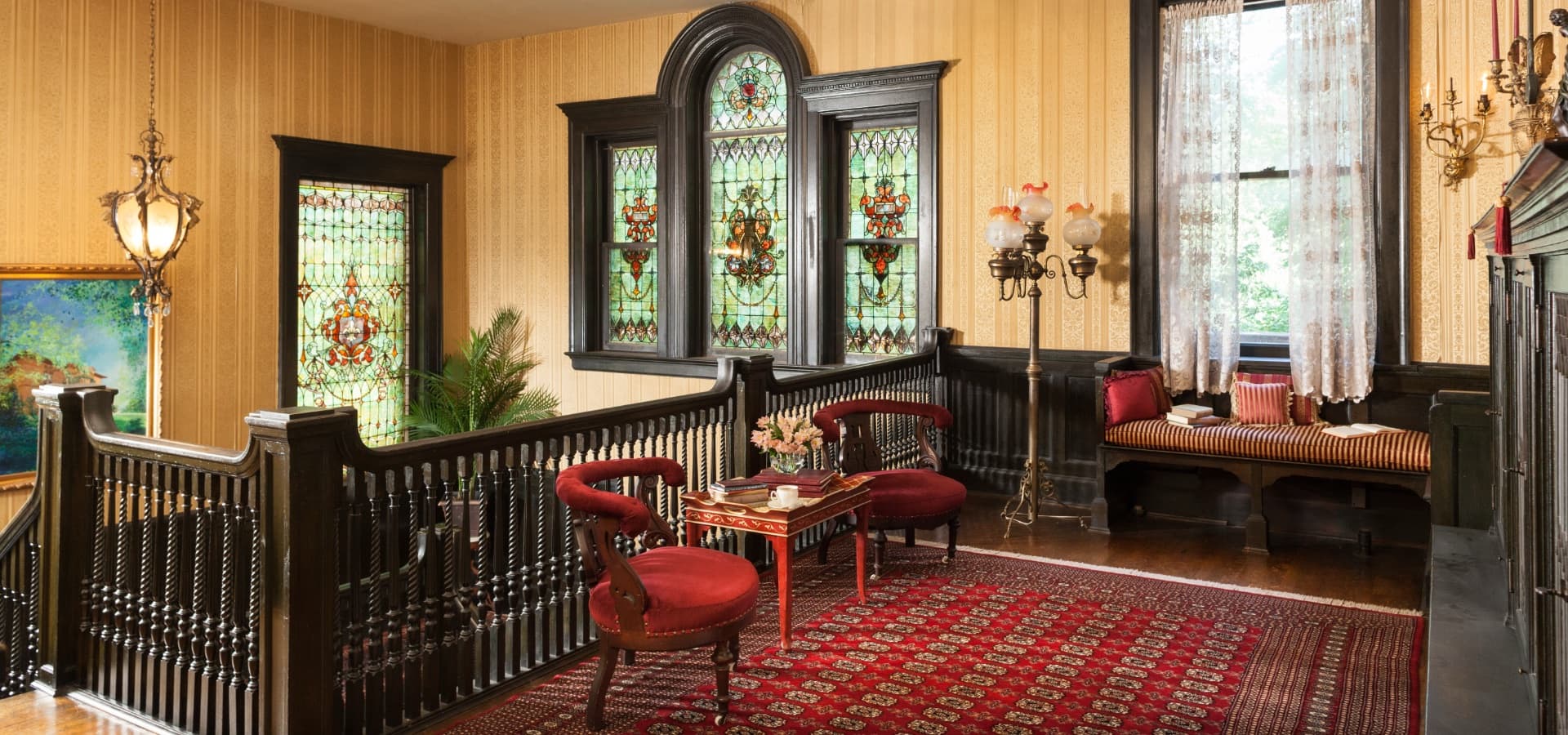 An elegantly decorated interior space featuring stained glass windows, plush red chairs, and a striking area rug.