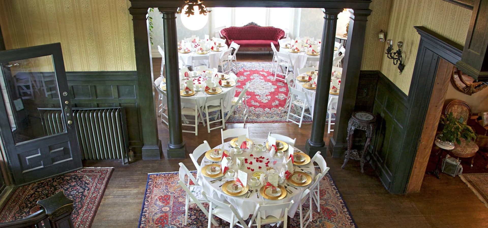 Elegant dining room set for a formal event, featuring round tables with white tablecloths and gold dinnerware.