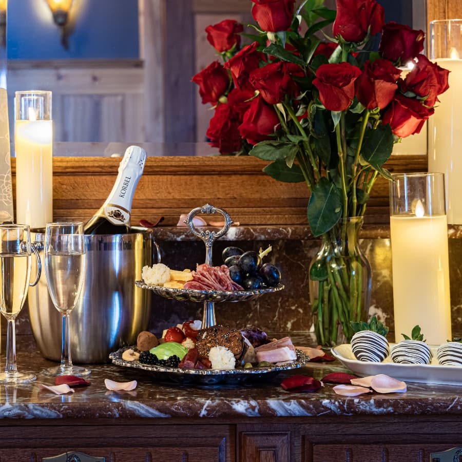 A romantic spread featuring a tiered tray of gourmet snacks, champagne, and roses.