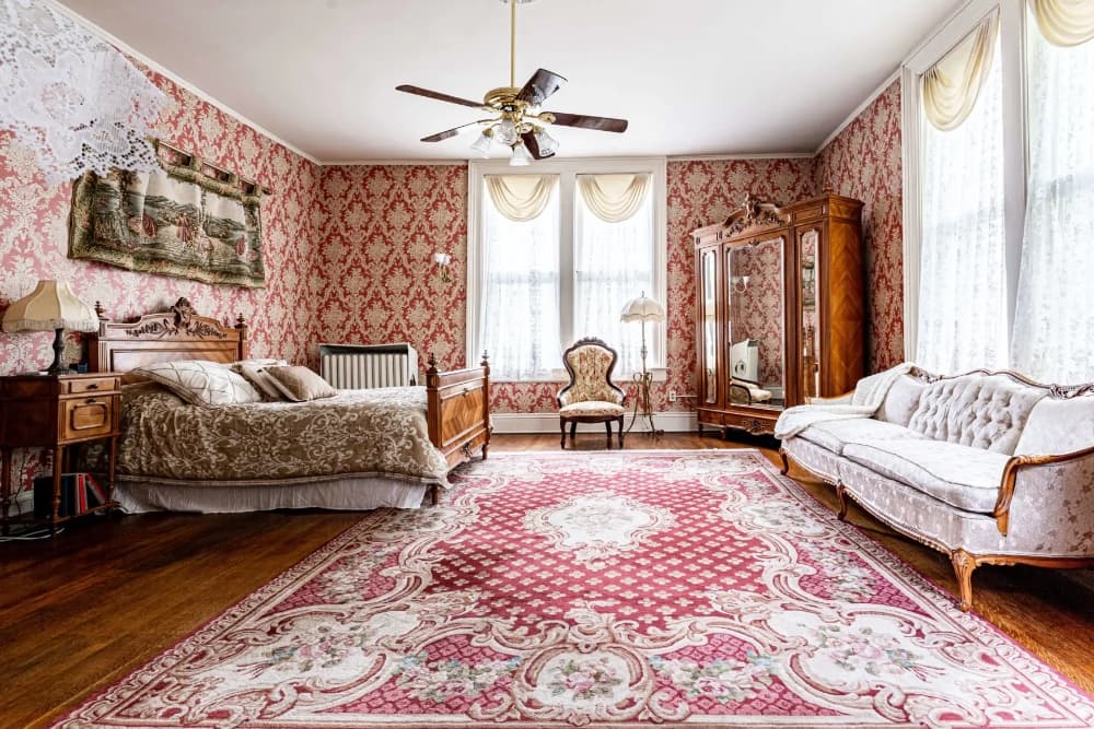 A vintage-style bedroom with ornate furniture, patterned wallpaper, and a decorative area rug.