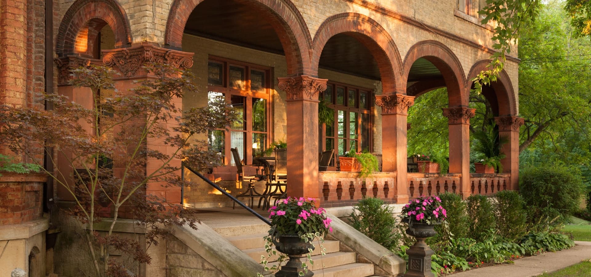 A historic porch features arched columns, potted plants, and a stone staircase adorned with flowers.